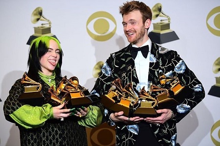 Billie Eilish sticking her tongue out with O'Connell, both holding the Grammys they won.